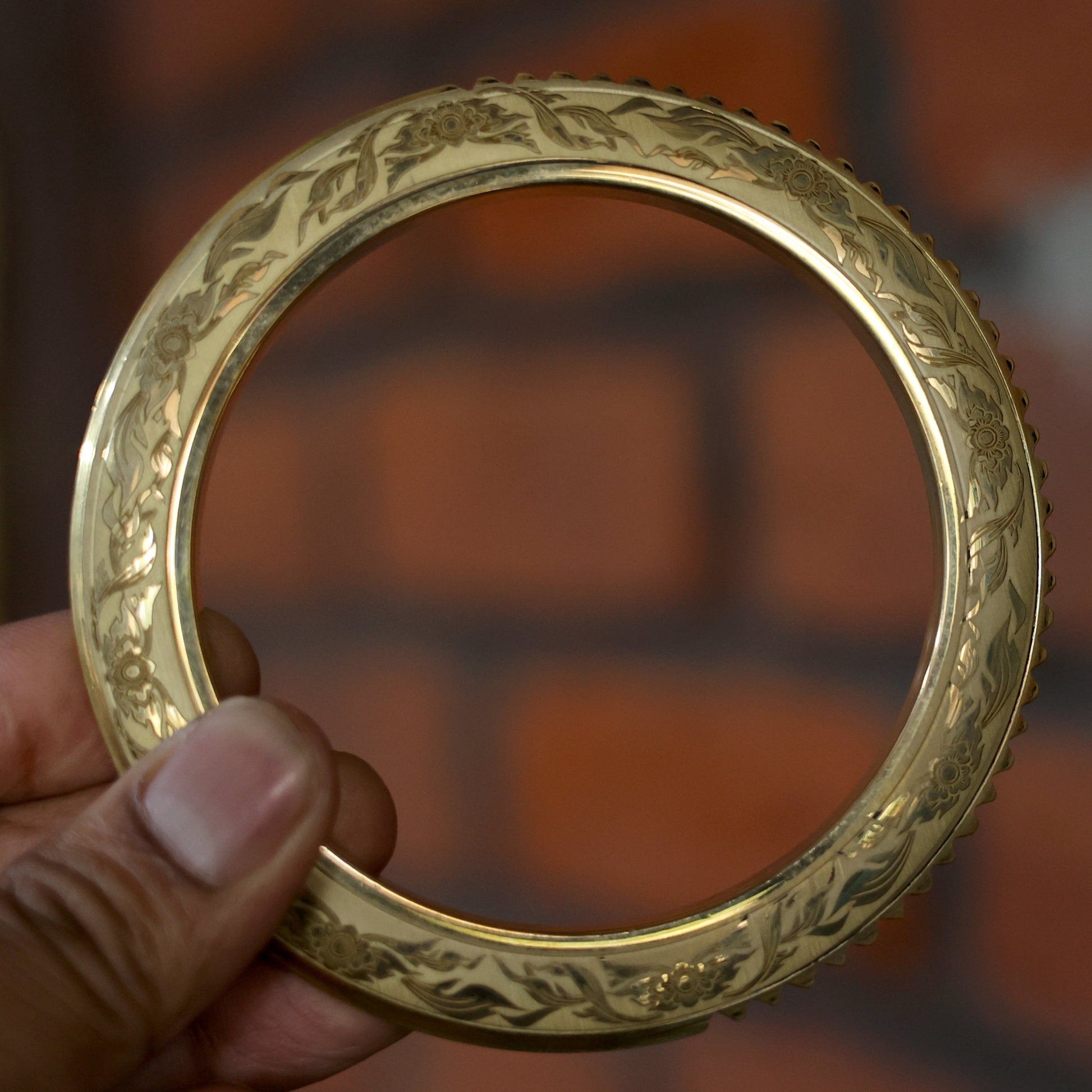Gold Kada held by a hand with a blurred brick wall background
